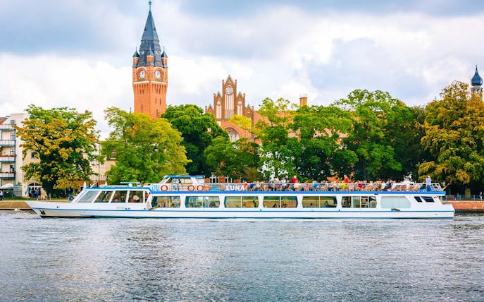 Cruise boat on Müggelsee lake with Berlin-Treptow church in background.