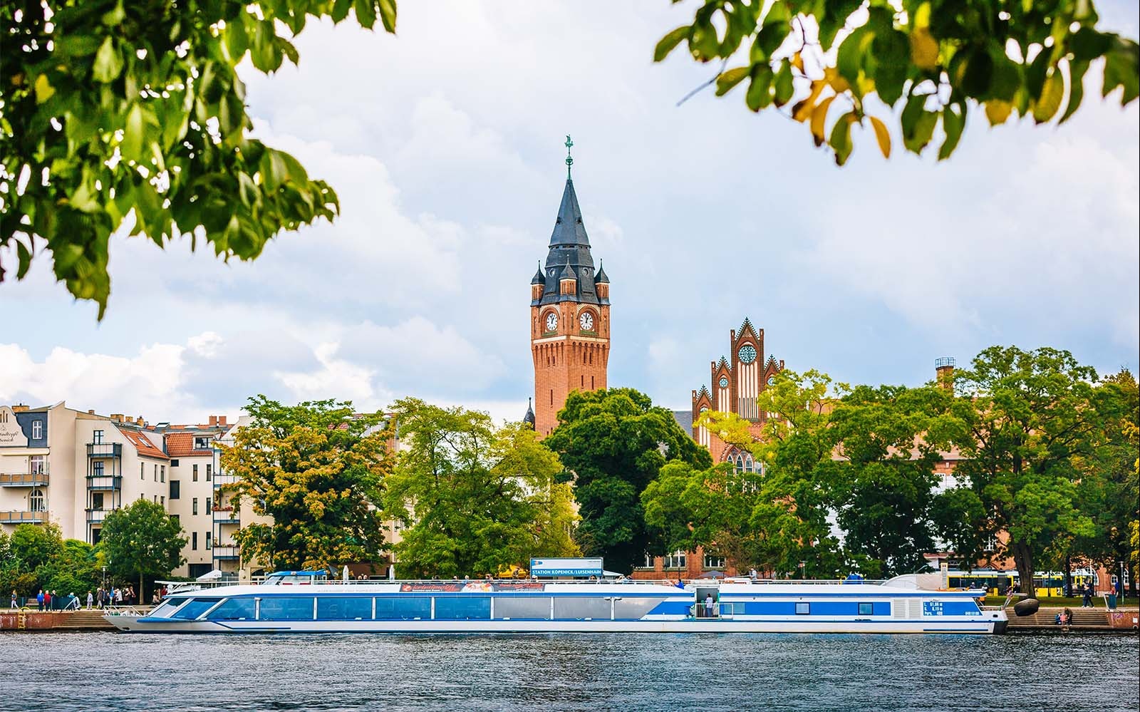 Cruise boat on Müggelsee lake with Berlin-Treptow's historic buildings in the background.