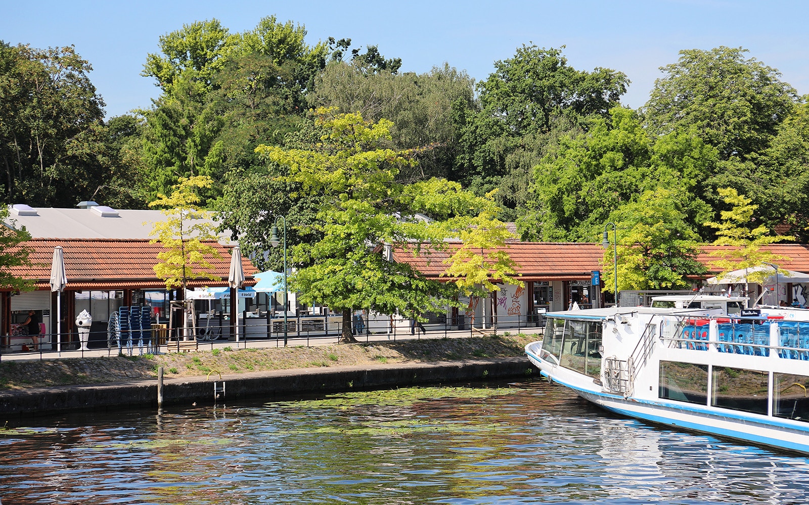 Cruise boat docked at Müggelsee lake with trees and buildings in Berlin-Treptow.