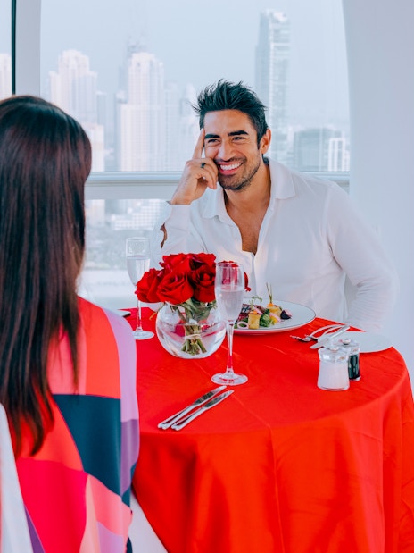 Couple dining with city view at Ain Dubai, red balloons and roses on table.