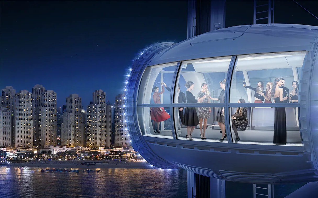 People enjoying a night view from Ain Dubai observation cabin, with city skyline in the background.