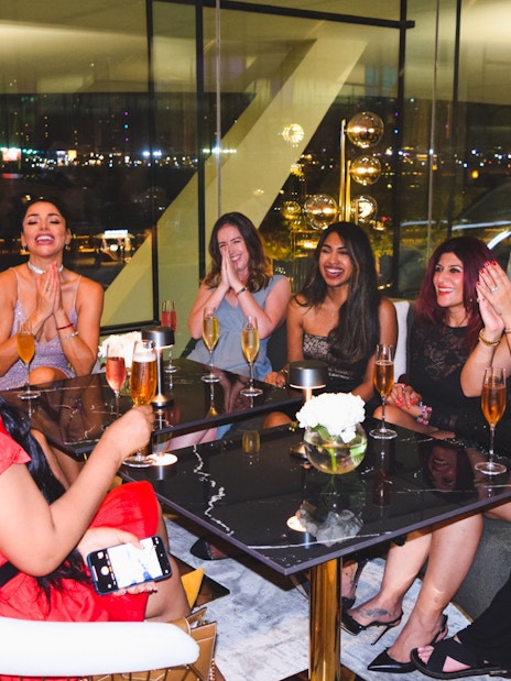 Group of friends enjoying drinks at a Dubai lounge with city lights in the background.