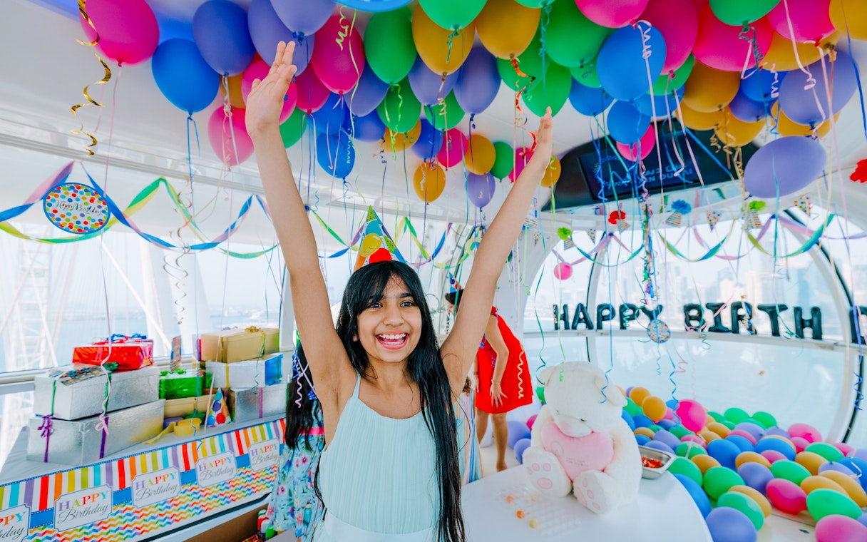Child celebrating birthday in Ain Dubai cabin with colorful balloons and decorations.
