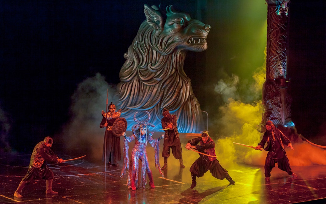 Performers in a dramatic scene at Bollywood Parks™ Dubai with a large wolf statue.