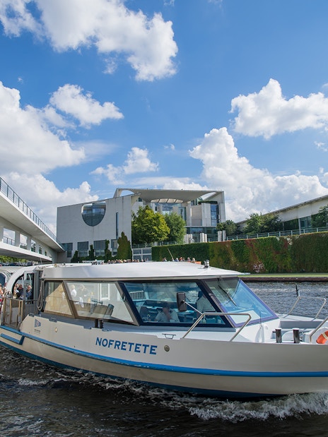 Boat cruising through Berlin's city center near modern architecture and bridge.
