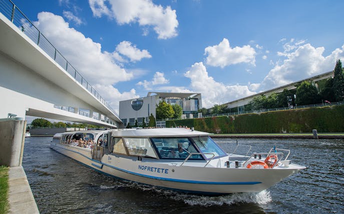 Boat cruising through Berlin's city center near modern architecture and bridge.
