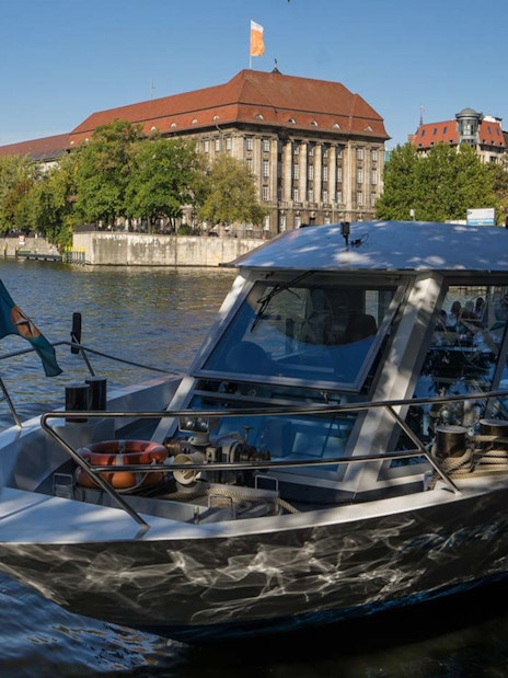 Boat docked on the Spree River in Berlin with historic buildings in the background.