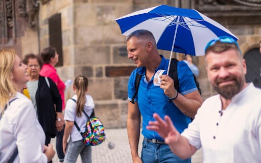 Tourists with guide at Prague Castle entrance, holding tickets and umbrella.