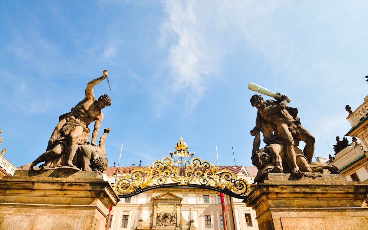 Prague Castle entrance statues with ornate gate under blue sky.