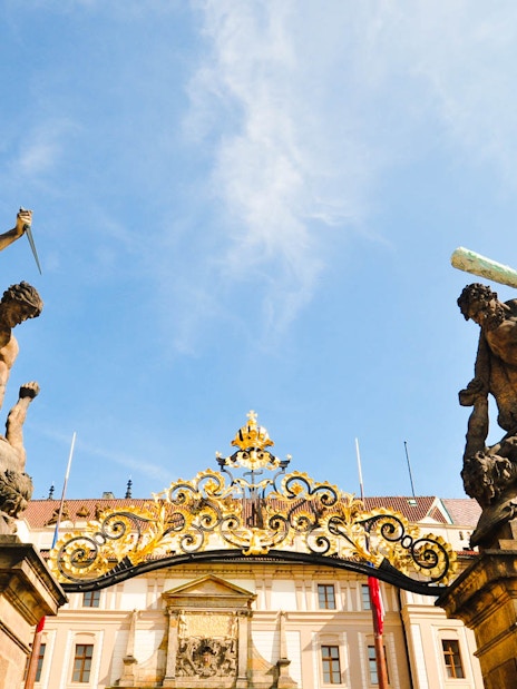 Prague Castle entrance statues with ornate gate under blue sky.