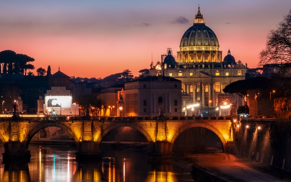 St. Peter's Basilica illuminated at sunset, Rome, viewed from a bridge during the Haunted Rome Ghost Tour.