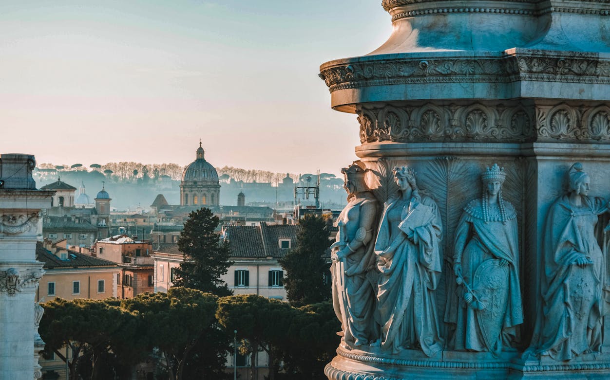Statues on a Roman building with cityscape and dome in the background, Rome ghost tour.