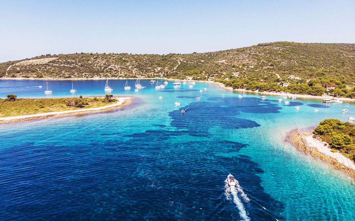 Boats sailing in the clear waters of Blue Lagoon near Split, Croatia, with lush green hills in the background.