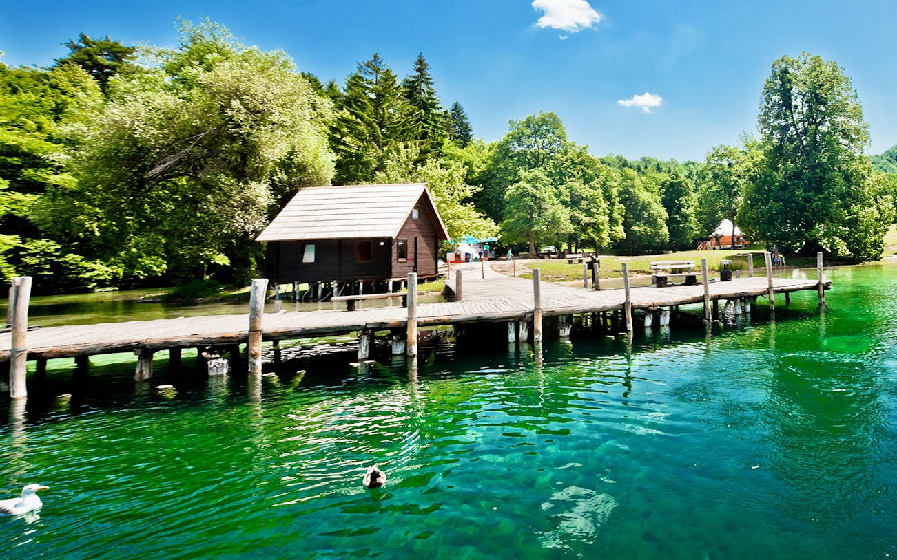 Wooden cabin and dock by a lush green lake in Split, Croatia.
