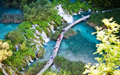 Visitors walking on a wooden path over turquoise lakes and waterfalls at Plitvice Lakes National Park.