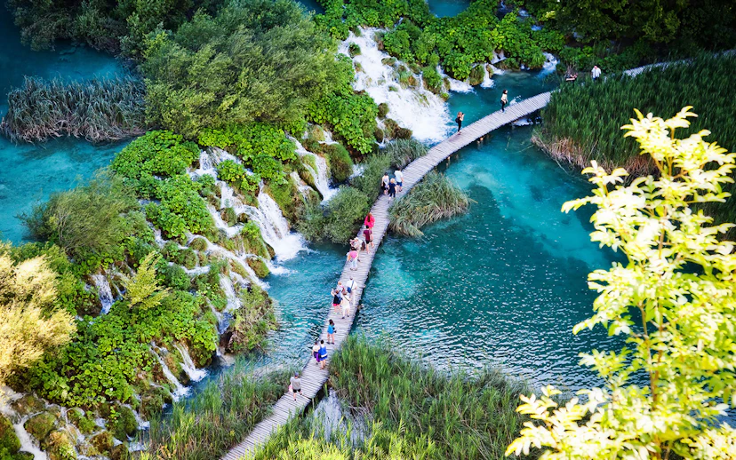 Visitors walking on a wooden path over turquoise lakes and waterfalls at Plitvice Lakes National Park.