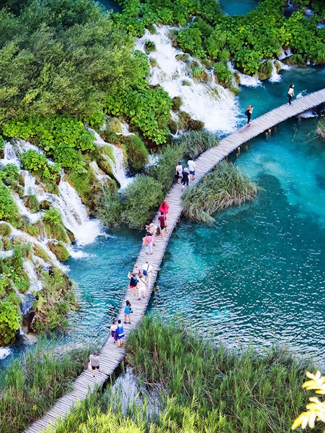 Visitors walking on a wooden path over turquoise lakes and waterfalls at Plitvice Lakes National Park.
