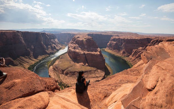 Person sitting on the edge overlooking Horseshoe Bend in Arizona with the Colorado River below.