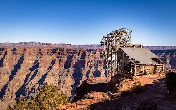 Old mining structure on the edge of the Grand Canyon West Rim under a clear blue sky.