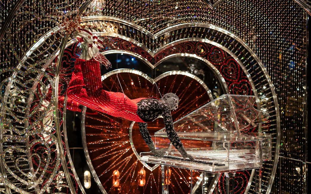 Performer in Swarovski Crystal Worlds display with crystal piano and heart backdrop.