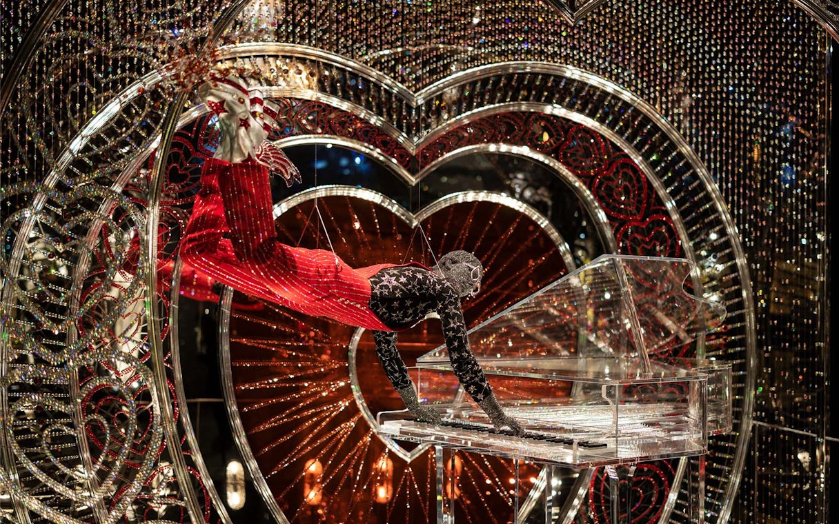 Performer in Swarovski Crystal Worlds display with crystal piano and heart backdrop.