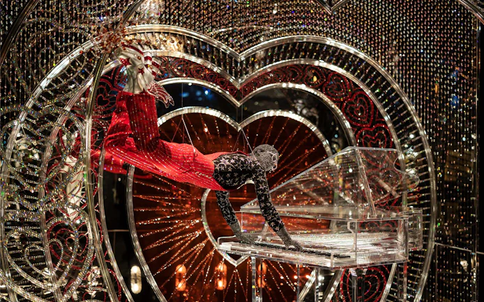 Performer in Swarovski Crystal Worlds display with crystal piano and heart backdrop.