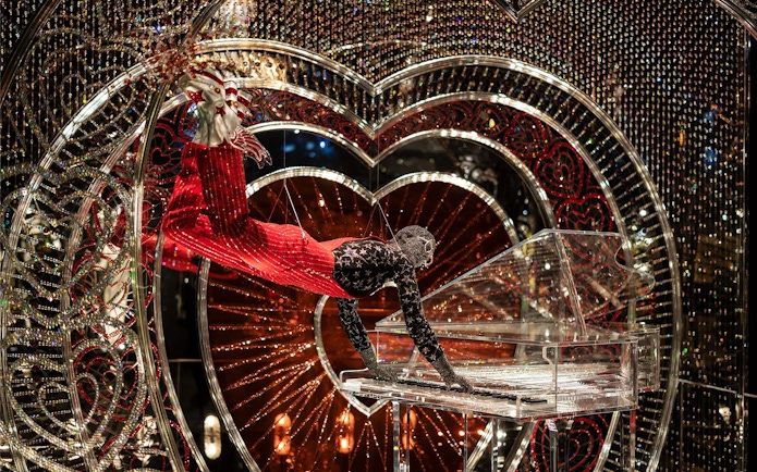 Performer in Swarovski Crystal Worlds display with crystal piano and heart backdrop.