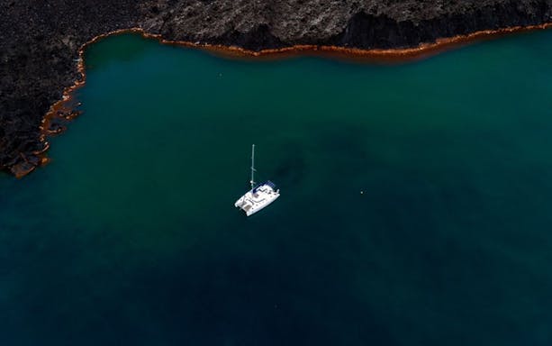 Catamaran sailing in Santorini caldera with rocky coastline.