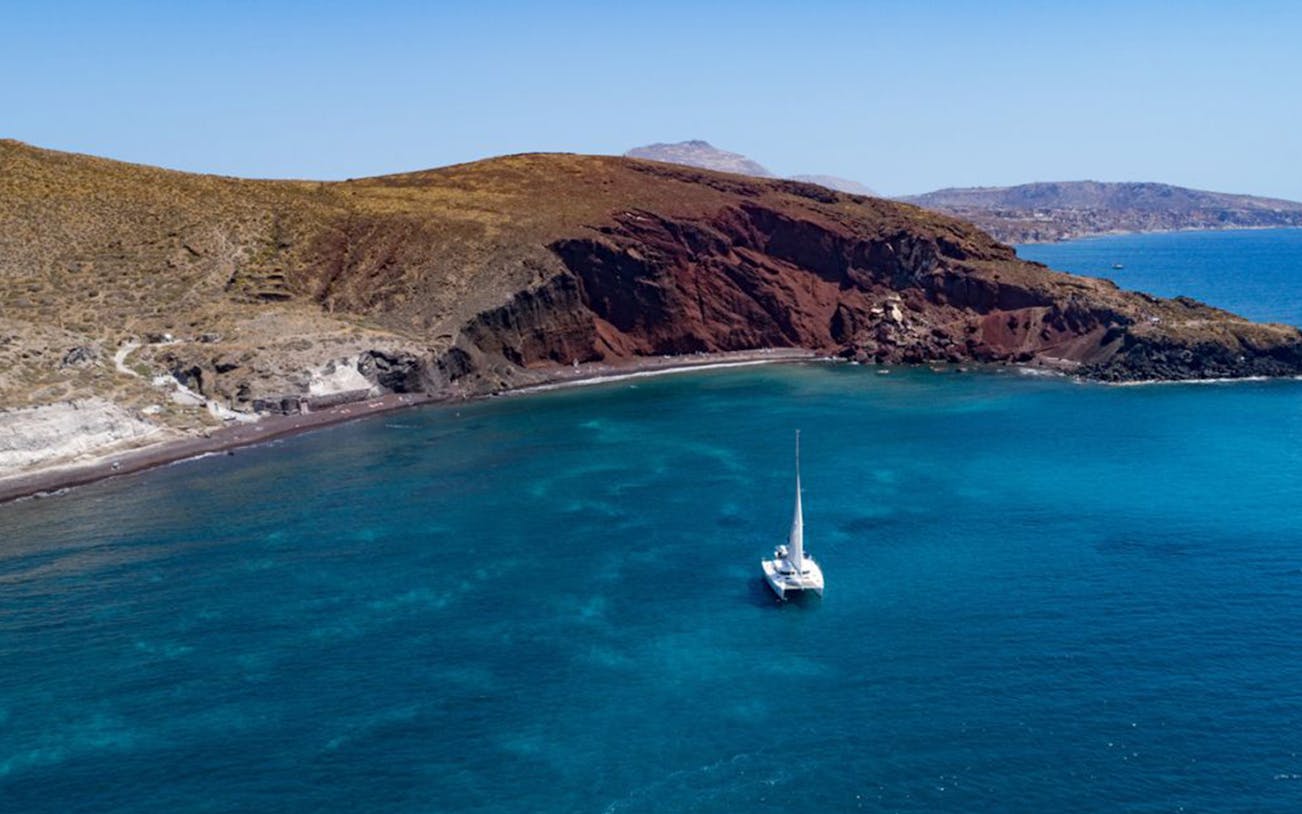 Catamaran sailing near Santorini's Red Beach during Caldera Day Cruise.