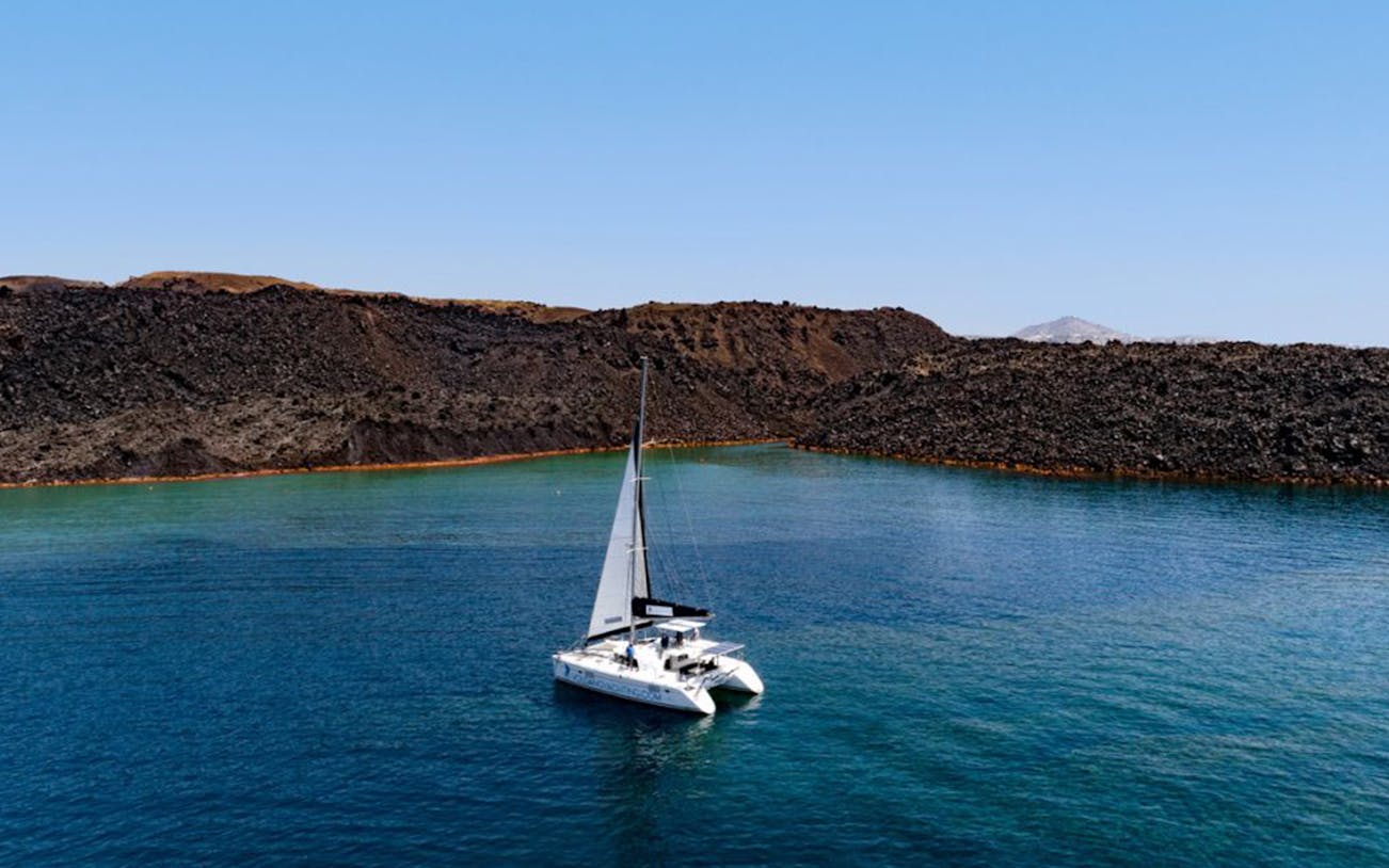 Catamaran sailing near volcanic cliffs in Santorini's caldera.