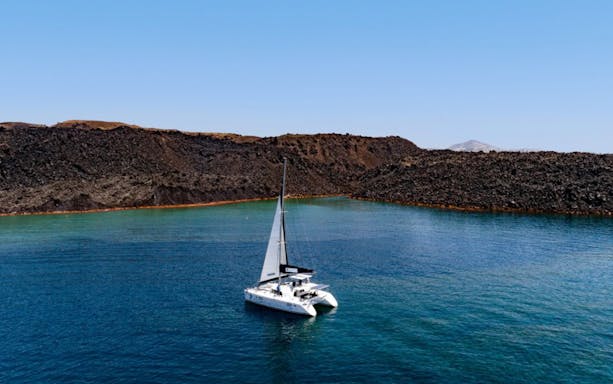 Catamaran sailing near volcanic cliffs in Santorini's caldera.