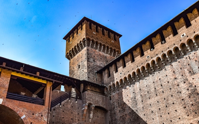 Sforza Castle brick tower and walls under a clear blue sky in Milan, Italy.