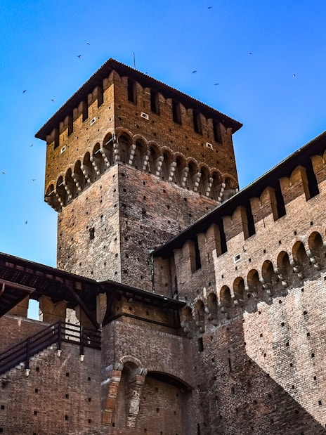 Sforza Castle brick tower and walls under a clear blue sky in Milan, Italy.