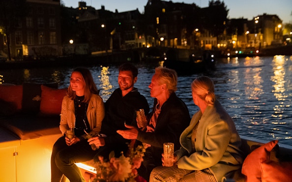 Evening cruise in Amsterdam with people enjoying drinks on a boat.