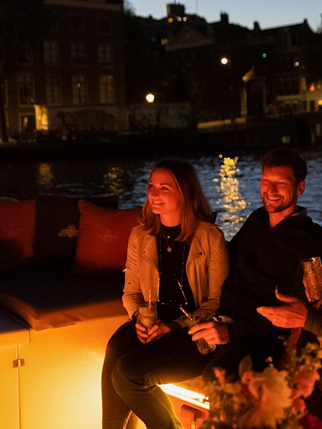 Evening cruise in Amsterdam with people enjoying drinks on a boat.