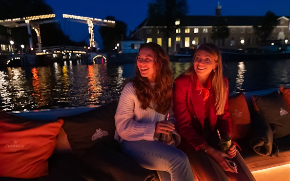 Evening canal cruise in Amsterdam with illuminated bridge in the background.