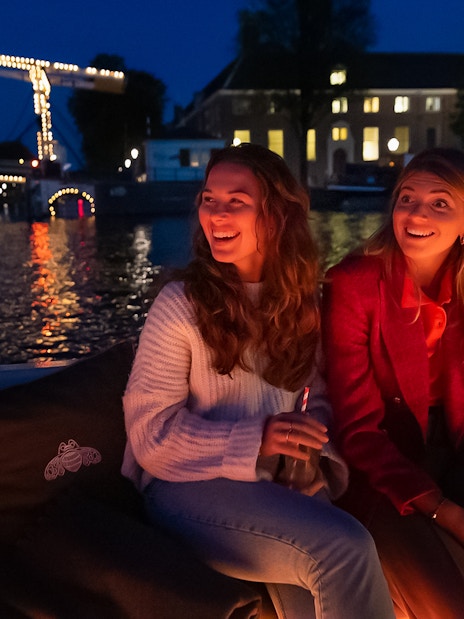 Evening canal cruise in Amsterdam with illuminated bridge in the background.