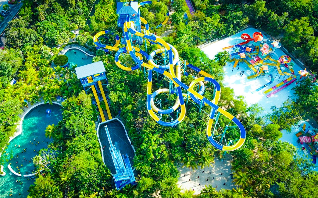 Aerial view of colorful water slides at ESCAPE Penang surrounded by lush greenery.