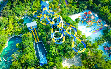 Aerial view of colorful water slides at ESCAPE Penang surrounded by lush greenery.