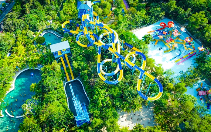 Aerial view of colorful water slides at ESCAPE Penang surrounded by lush greenery.