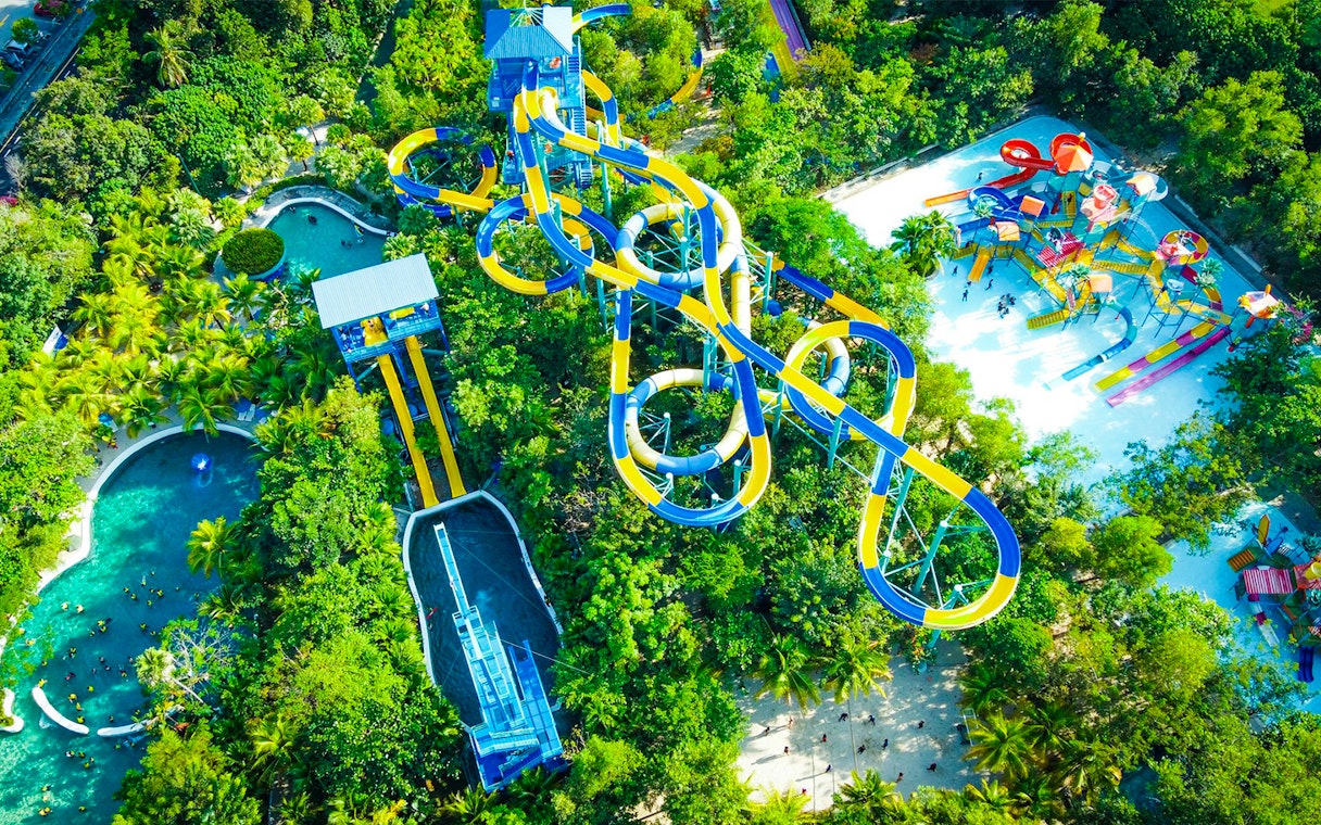 Aerial view of colorful water slides at ESCAPE Penang surrounded by lush greenery.