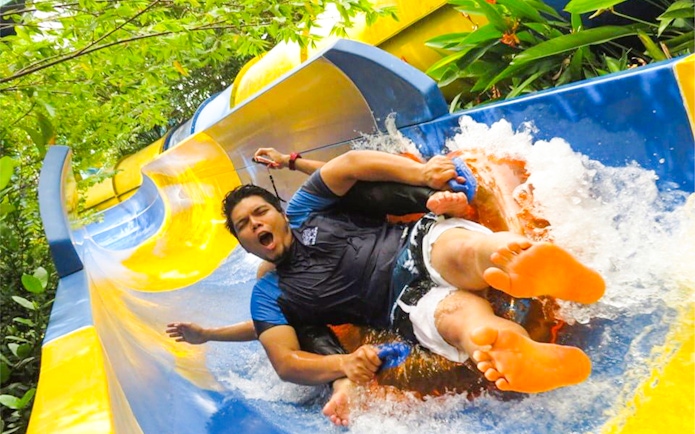 Man enjoying water slide at ESCAPE Penang, surrounded by lush greenery.