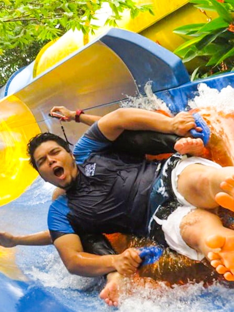 Man enjoying water slide at ESCAPE Penang, surrounded by lush greenery.
