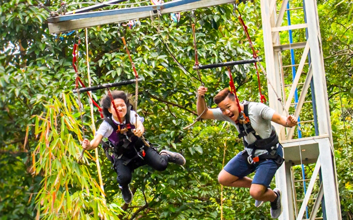 Visitors enjoying a zip line ride at ESCAPE Theme Park, Penang, surrounded by lush greenery.