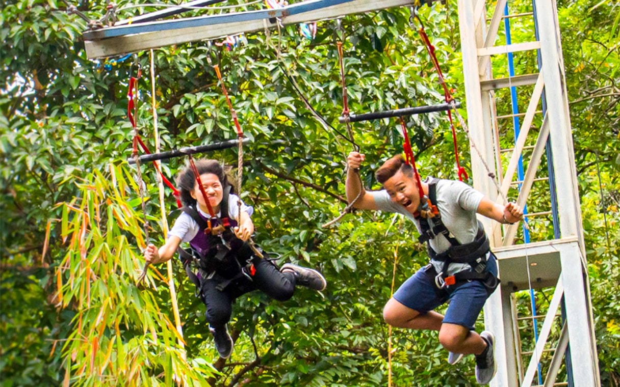 Visitors enjoying a zip line ride at ESCAPE Theme Park, Penang, surrounded by lush greenery.