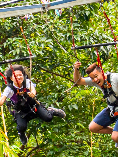 Visitors enjoying a zip line ride at ESCAPE Theme Park, Penang, surrounded by lush greenery.