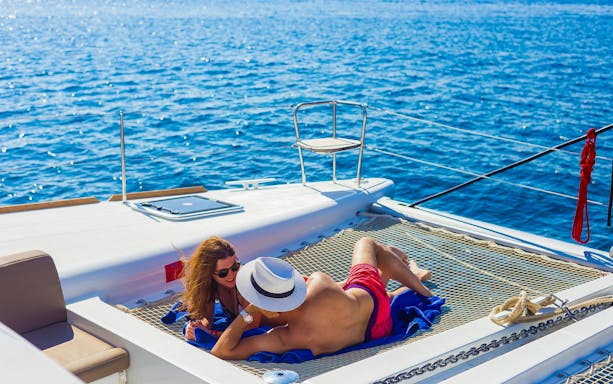 Couple relaxing on a catamaran net during a Santorini sailing cruise.