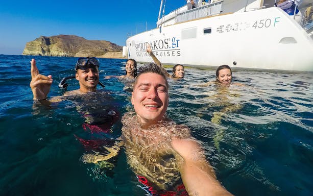 Group enjoying a swim near a catamaran during a Santorini sailing cruise.