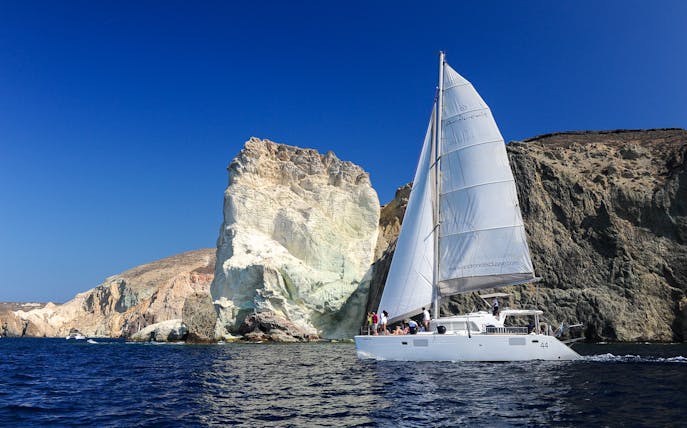 Catamaran sailing near cliffs in Santorini, Greece.