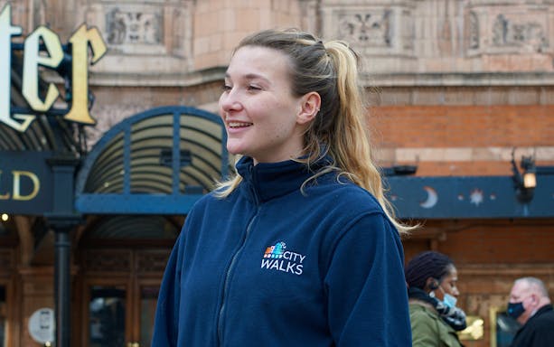 Guide in City Walks jacket near London theater entrance.